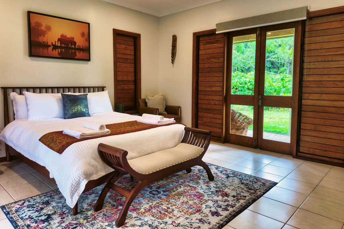 A bedroom with a bed, a chair, a window, and a painting on the wall.
