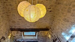 Interior rústico de pedra com um lanternim de papel pendurado, um banco de madeira e uma pequena mesa com um saco de plástico.