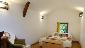 Um quarto pequeno e acolhedor com uma cama de casal, um penteado de madeira, uma poltrona verde e duas luzes fixadas na parede.