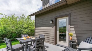 Une terrasse extérieure avec une table et des chaises, une porte et une vue sur la végétation environnante.