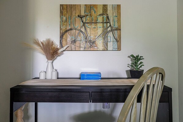 Un bureau avec un plateau en bois, un vase contenant des plantes séchées, une plante en pot et un livre bleu.