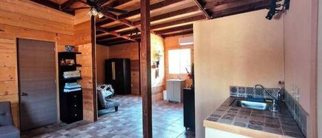 A wooden cabin interior with a kitchen area, a dining table, and a sofa.