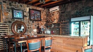 Una zona de bar rústica con mobiliario de madera, paredes de piedra y una estantería para vinos.