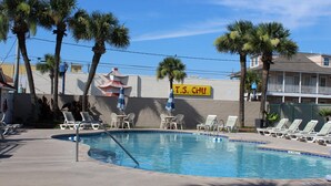 A pool area with lounge chairs and umbrellas, palm trees, and a T.S. CHU sign. - Charming 2 bedroom 2 bath condo, sleeps 6 with WiFi, AC on wonderful Tybee Isl. (Tybee Island)