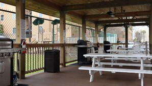 An outdoor patio area with picnic tables, a barbecue grill, and a trash bin. - Charming 2 bedroom 2 bath condo, sleeps 6 with WiFi, AC on wonderful Tybee Isl. (Tybee Island)