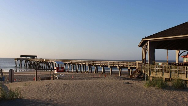 A beach with a wooden pier extending into the sea, a covered seating area, and a lifeguard stand. - Charming 2 bedroom 2 bath condo, sleeps 6 with WiFi, AC on wonderful Tybee Isl. (Tybee Island)