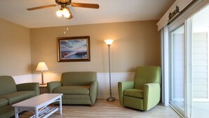 A living room with two green armchairs, a white coffee table, a floor lamp, a ceiling fan, and a framed picture on the wall. - Charming 2 bedroom 2 bath condo, sleeps 6 with WiFi, AC on wonderful Tybee Isl. (Tybee Island)