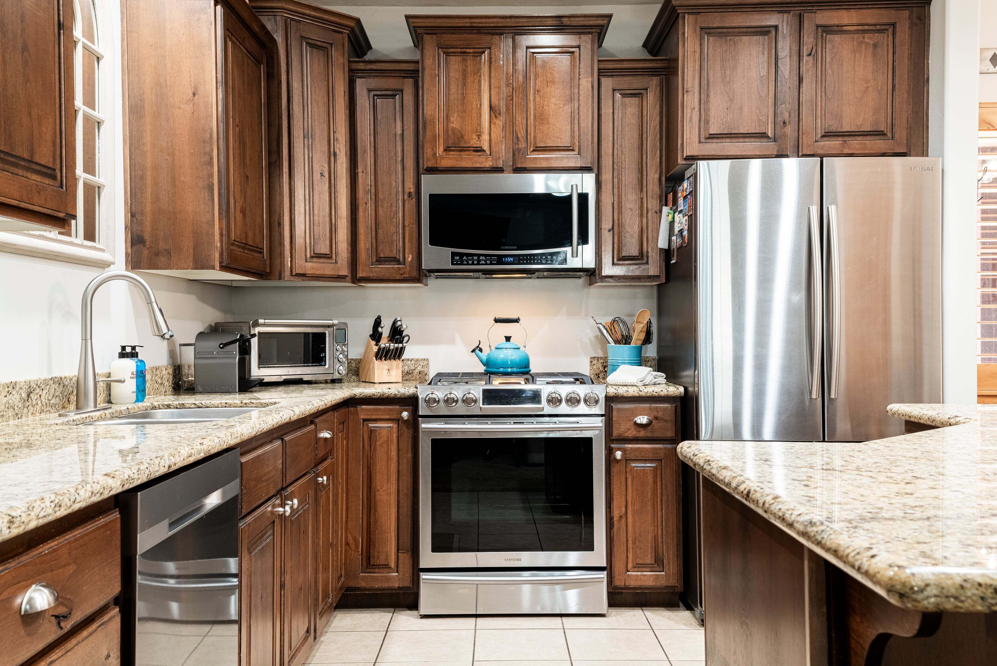A kitchen with wooden cabinets, stainless steel appliances, granite countertops, and a blue kettle.
