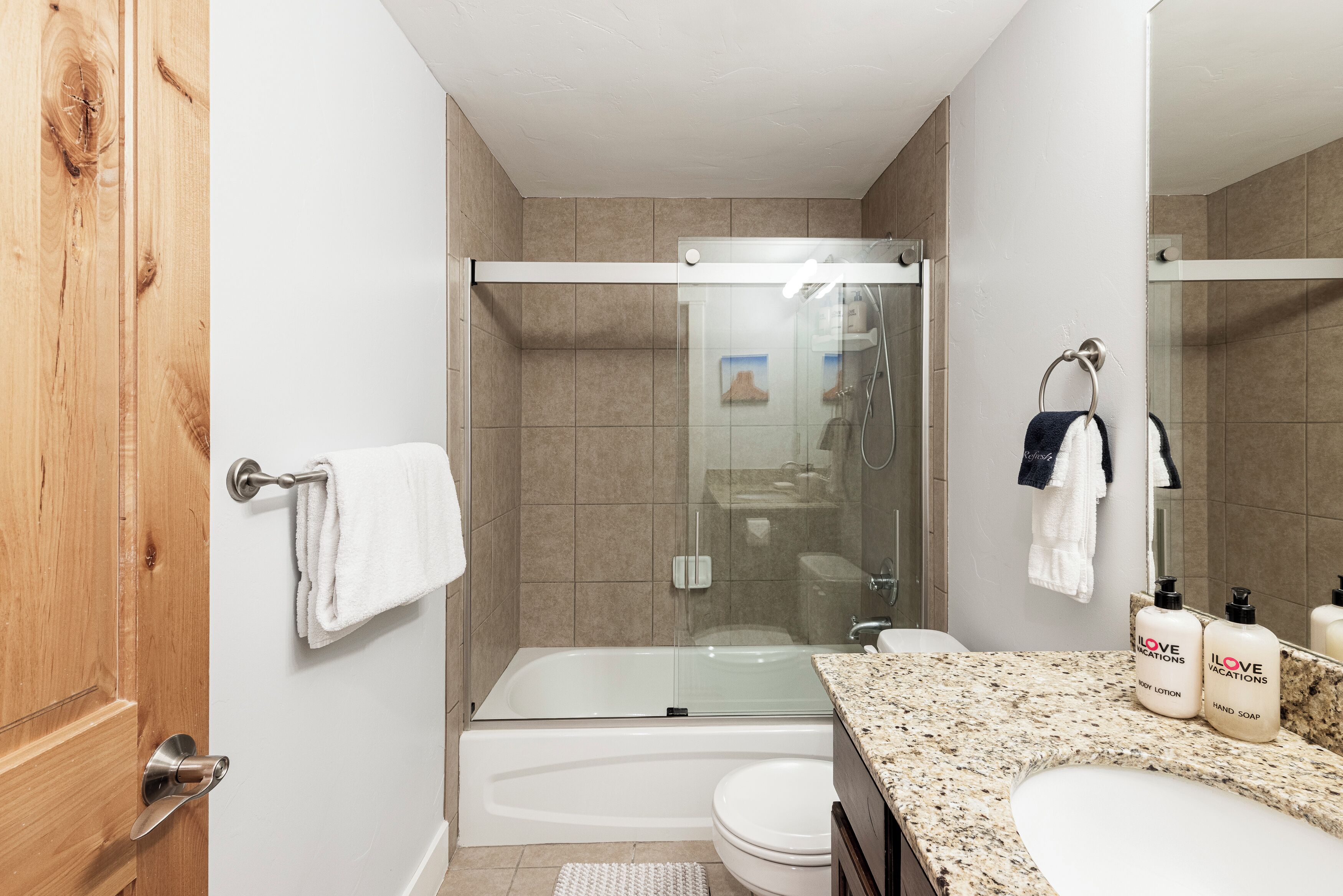 A modern bathroom with a glass-enclosed shower, a standalone bathtub, and a vanity with a granite countertop.