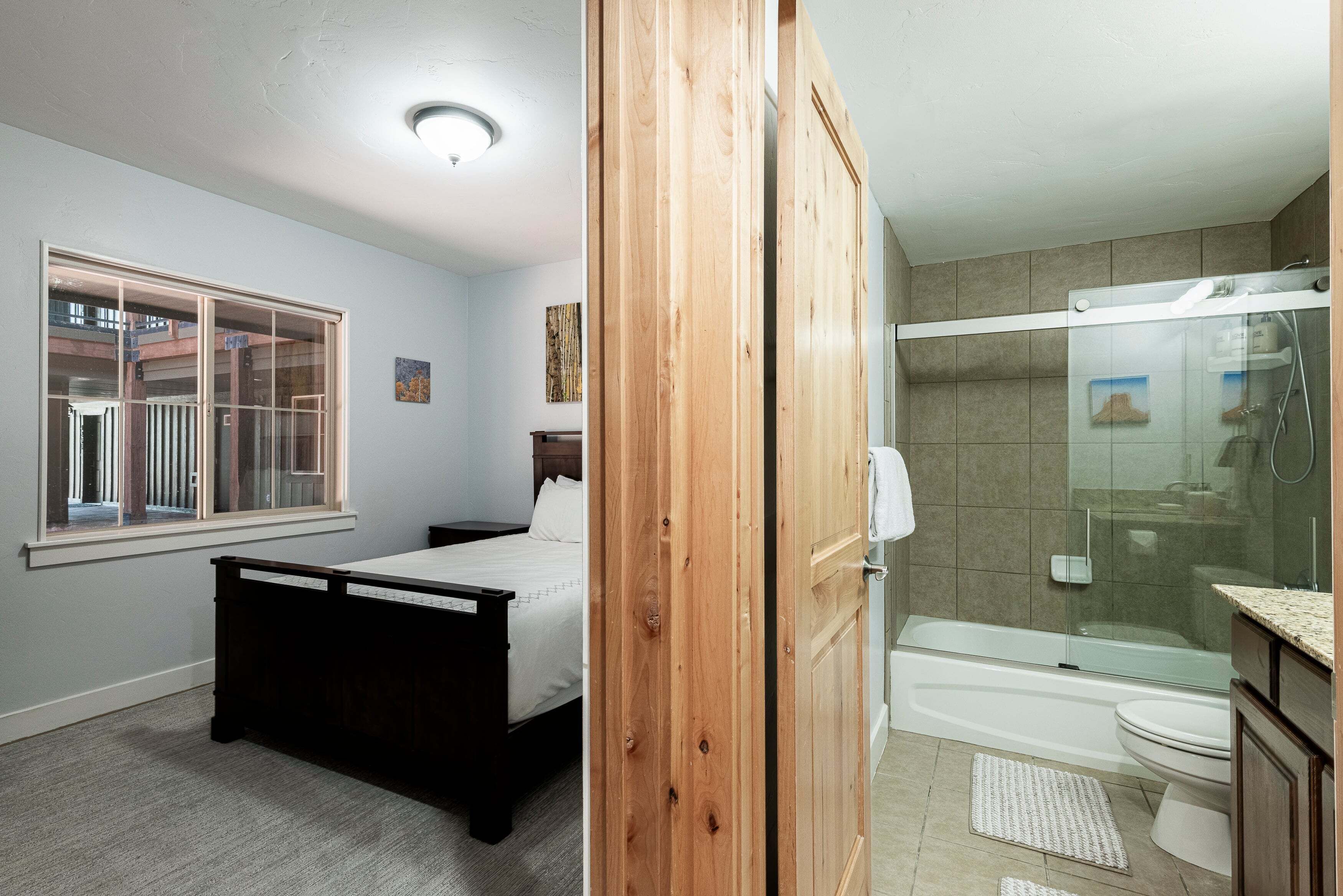 A bedroom with a bed, a window, and a bathroom with a shower and toilet.