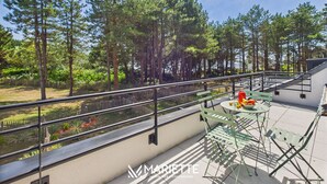 Un balcón con vistas a un bosque, una mesa con frutero y una barandilla de metal.