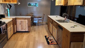 A modern kitchen with wooden cabinets, a central island, and a dining area. - Escape to the Woods! Farmhouse on 10 acres -Great Wifi, Big Kitchen. BOOK IT! (Saint Regis Falls)