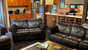 A living room with two leather sofas, a coffee table, and a kitchen in the background. - Escape to the Woods! Farmhouse on 10 acres -Great Wifi, Big Kitchen. BOOK IT! (Saint Regis Falls)