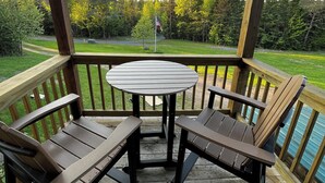 A covered outdoor seating area with a table and chairs, overlooking a grassy landscape and a flagpole. - Escape to the Woods! Farmhouse on 10 acres -Great Wifi, Big Kitchen. BOOK IT! (Saint Regis Falls)