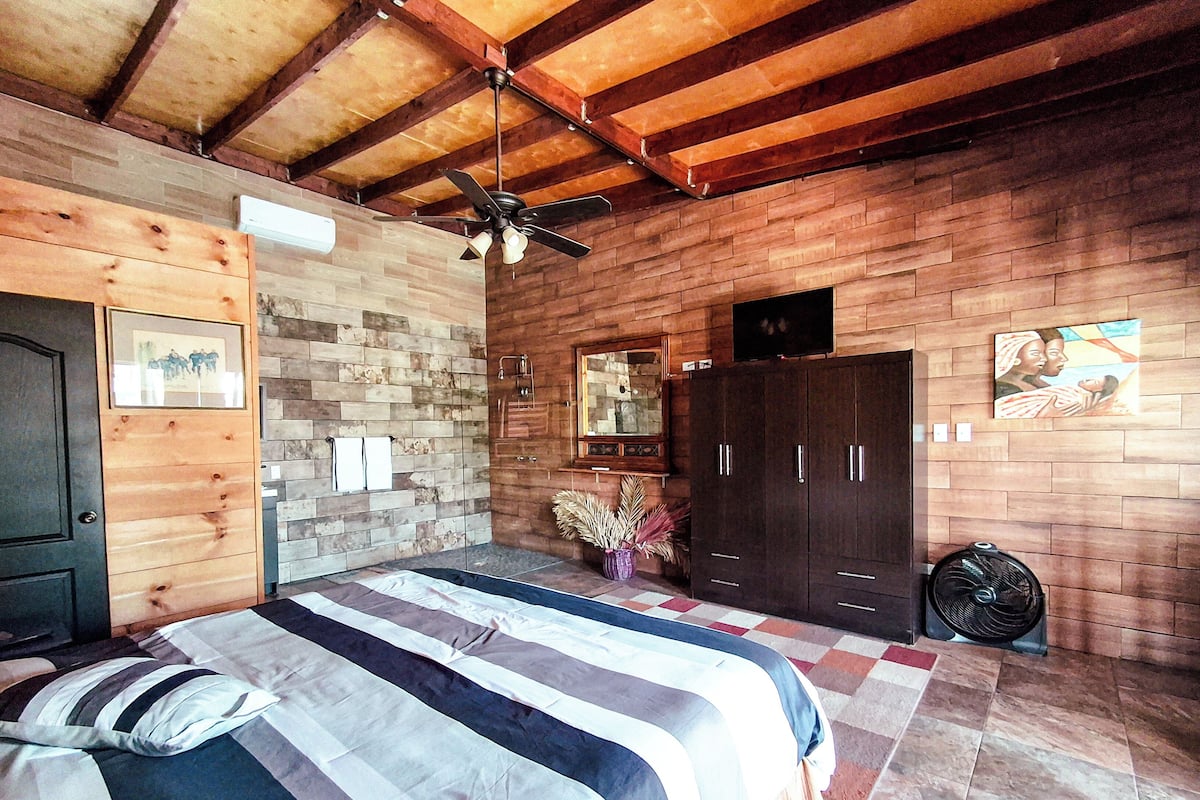 A bedroom with two beds, a wooden ceiling, a stone wall, a mirror, and a wardrobe.