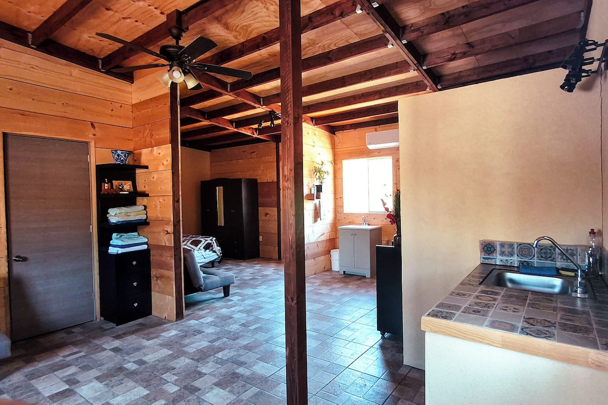 A log cabin interior with a tiled floor, a ceiling fan, a kitchenette, and a small seating area.