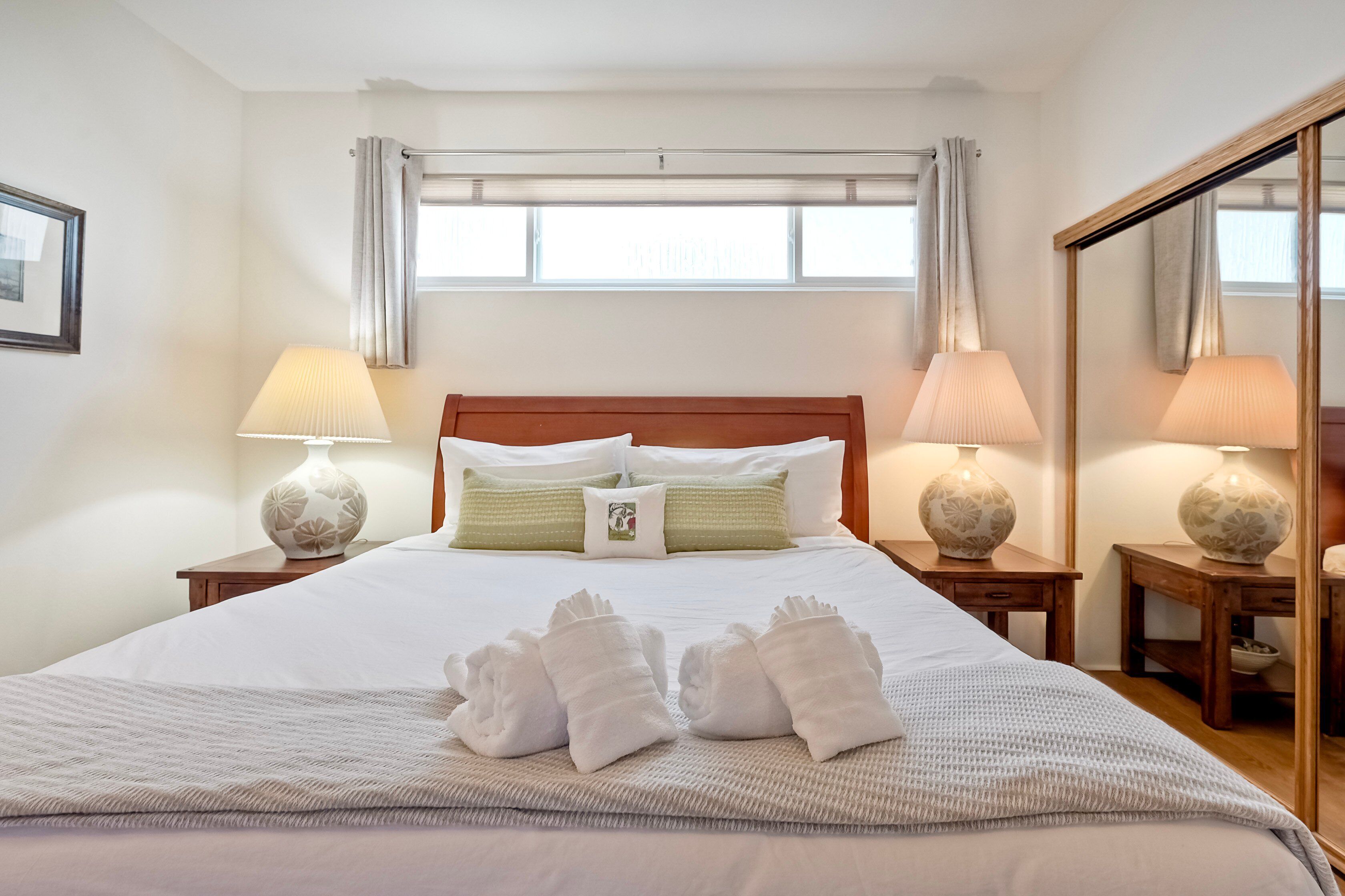 A neatly made bed with white linens, two bedside lamps, and a window with curtains.