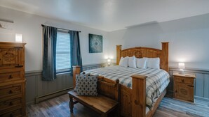 A bedroom with a wooden bed, bedside tables, a bench, a window with curtains, and a wall-mounted artwork. - Recently-renovated condo across from the Fox shuttle stop! (Angel Fire)