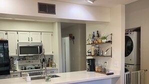A modern kitchen with white cabinets, a microwave, and a built-in oven. There are bar stools and a woven round table. - Modern, Peaceful Tempe Condo • Pool & Fast Wi-Fi (Tempe)