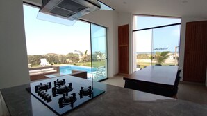 Una habitación moderna con un amplio ventanal que da a una zona de piscina, una mesa de comedor y un equipo de aire acondicionado instalado en el techo.