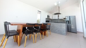 Una cocina moderna con una isla central, un comedor con mesa de madera y sillas negras, y un refrigerador empotrado.