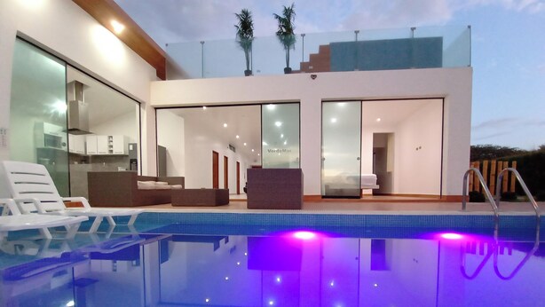 Una casa moderna con piscina, puertas de vidrio que dan a una sala de estar y una cocina a la vista.