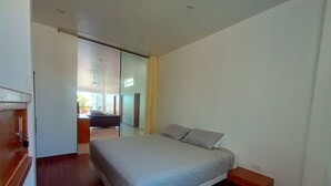 Un dormitorio con cama, piso de madera, una puerta corredera y vistas a otra habitación.