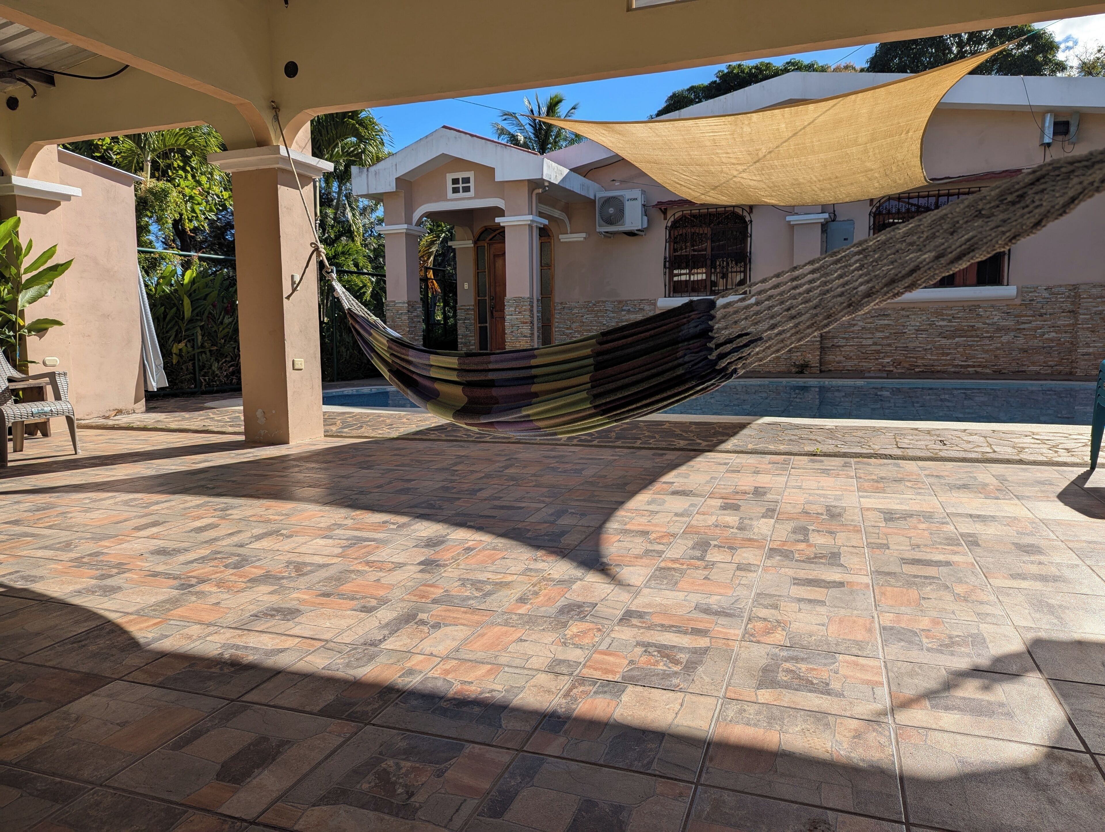A hammock hanging between two columns in an outdoor patio area with tiled flooring and a shaded canopy.