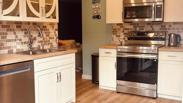 Une cuisine moderne avec des armoires blanches, des appareils en acier inoxydable et un plancher en bois.