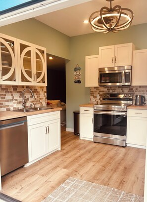 A modern kitchen with white cabinets, stainless steel appliances, and a wooden floor.
