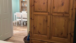 Une chambre avec une grande armoire en bois, un lit avec une literie blanche, et un coin repas à l’arrière-plan.