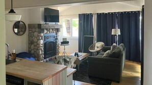 A living room with a stone fireplace, a television, a dining area with a table and chairs, and a sofa.