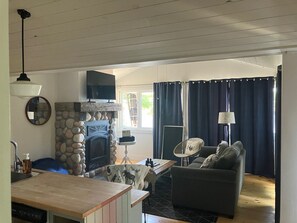 Uma sala de estar com lareira de pedra, televisão, área de refeições com mesa e cadeiras, e um sofá.