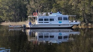 A houseboat with a covered deck, windows, and a small cabin area. - Houseboat Hire Myall Lakes National Park NSW (Bulahdelah)