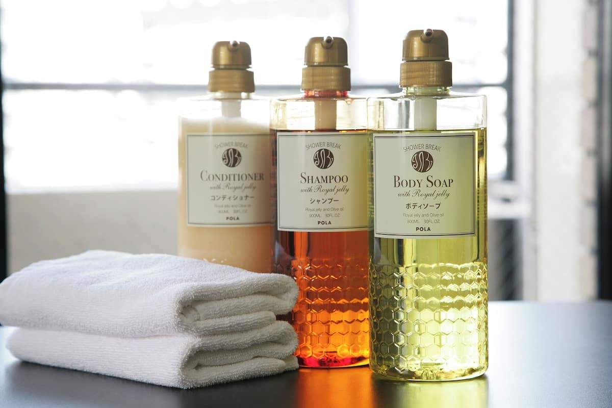 Three bottles of shower products on a table with a folded white towel.