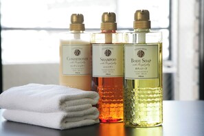 Three bottles of shower products on a table with a folded white towel. - Axion Hotels Tenjin (Fukuoka)