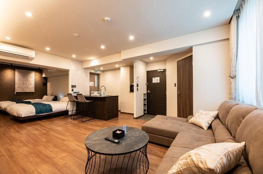 A modern hotel room with a bed, a sofa, a small dining area, and a kitchenette.