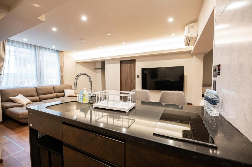 A modern living room with a dark-toned kitchen island, a sofa, and a flat-screen TV.