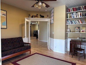 A living room with a sofa, a bookshelf, a piano, and a ceiling fan.