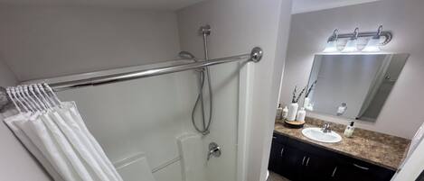Un baño moderno con cabina de ducha de vidrio, tocador con lavabo y espejo sobre el lavabo.
