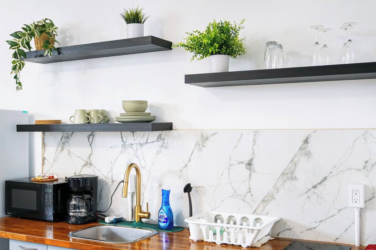 A kitchen with a marble backsplash, a sink, a coffee maker, and a microwave.