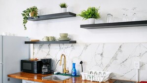A kitchen with a marble backsplash, a wooden countertop, a sink, a microwave, a coffee maker, and two black shelves with plants and kitchenware. - CARIBBEAN STARS (Carolina)