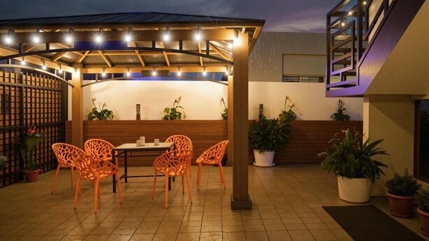 An outdoor patio with a wooden pergola, orange chairs, a table, and potted plants. - CARIBBEAN STARS (Carolina)
