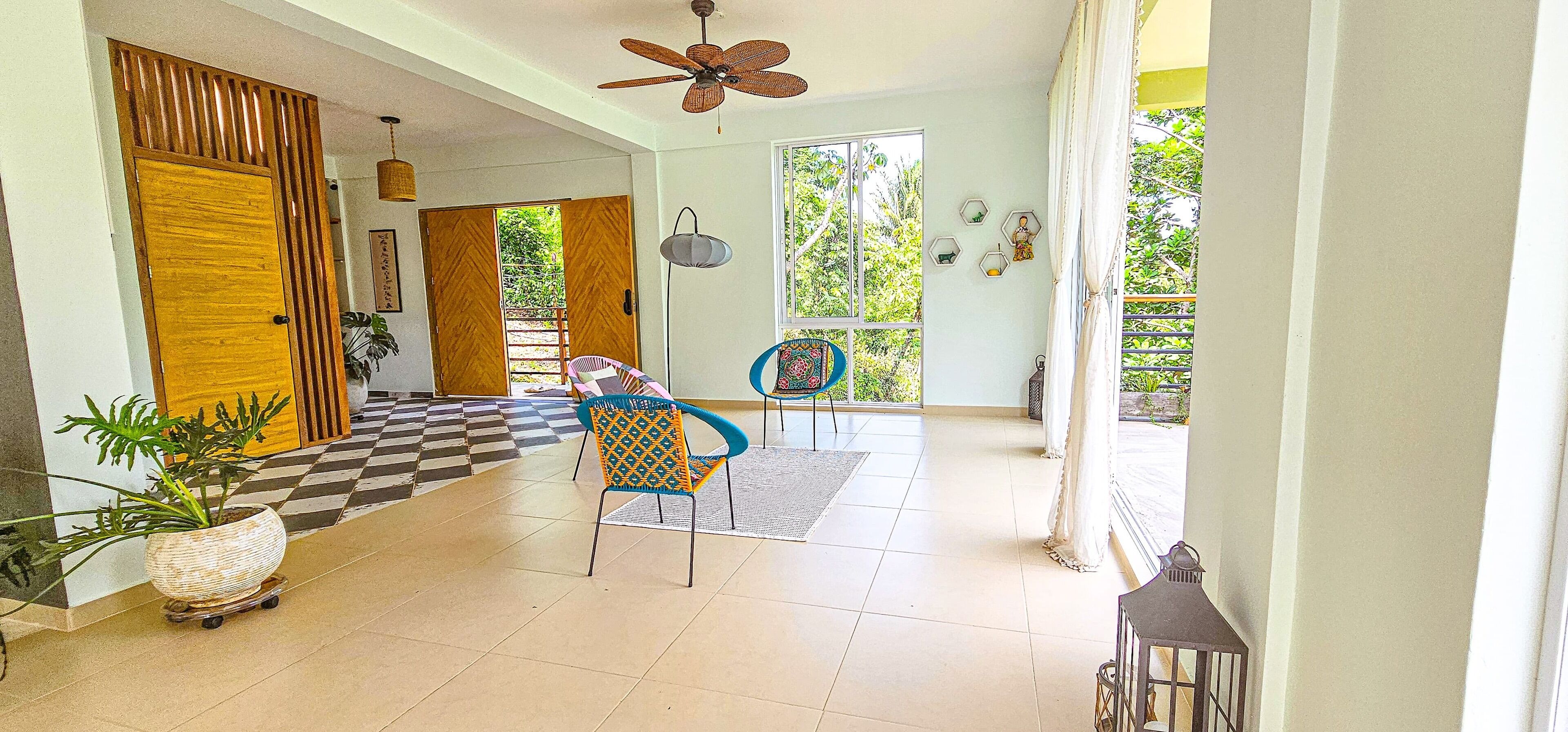 Un vaste espace intérieur doté d’un sol à carreaux, d’un ventilateur de plafond et offrant une vue sur la verdure environnante.