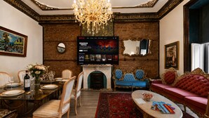 Een kamer met een open haard, een televisie waarop een programma draait, een eettafel gedekt voor zes personen, en een rode bank.
