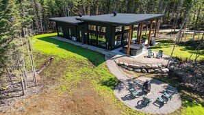 A modern cabin with a large deck, surrounded by a forest.