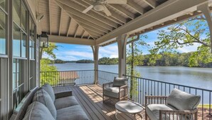 A covered outdoor deck with a view of a lake, furnished with sofas and wicker chairs. - Experience Ultimate Relaxation: Stunning Lakeside Retreat (Dadeville)