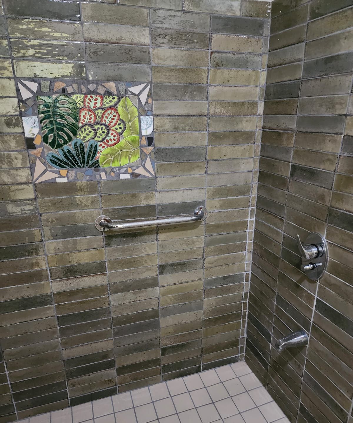 Uma área de chuveiro com design em mosaico, barra de apoio e piso revestido.