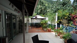 An outdoor patio area with a covered seating area, potted plants, and a view of a hillside.