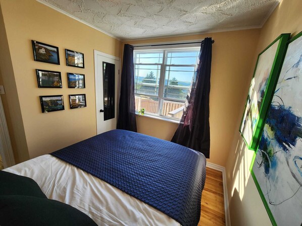 A bedroom with a bed, a window with curtains, and several framed pictures on the wall.